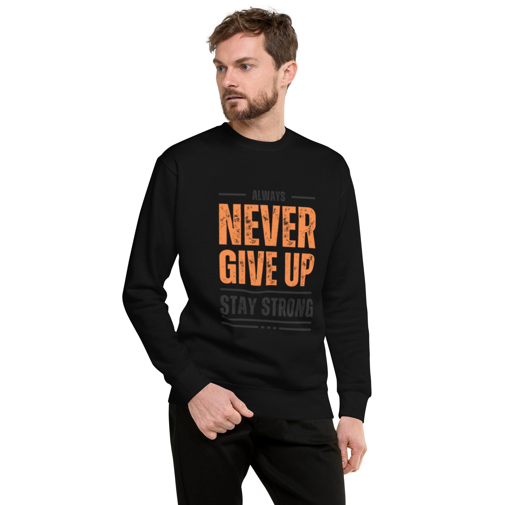 A man with light brown hair and a beard models the Never Give Up Unisex Premium Sweatshirt, featuring orange and gray “ALWAYS NEVER GIVE UP STAY STRONG” text. He stands with one hand in his pocket, embodying modern streetwear style.