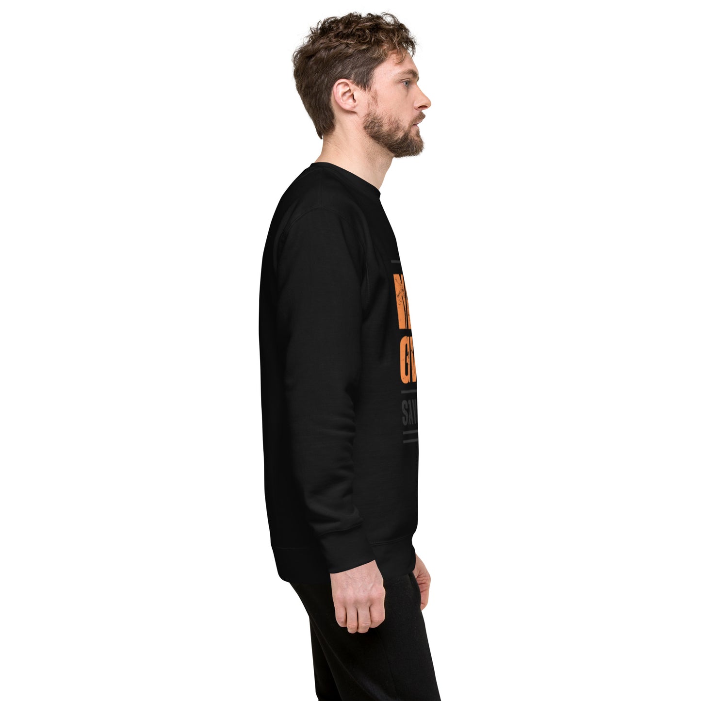 A man with light brown hair and a beard stands in profile, wearing the Never Give Up Unisex Premium Sweatshirt and black pants against a white background. The bold orange and white text adds a modern streetwear vibe.
