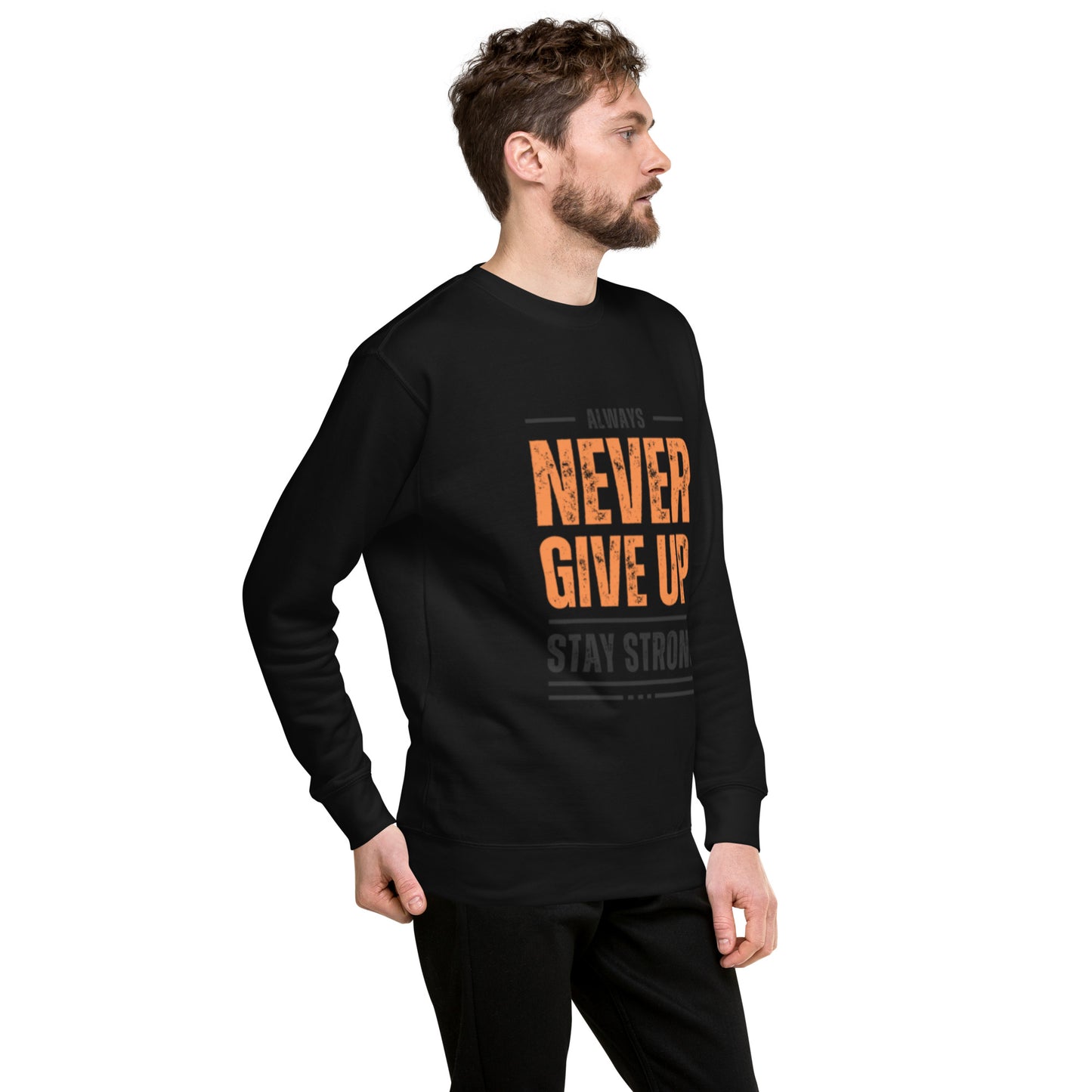 A man with short curly hair and a beard wears the Never Give Up Unisex Premium Sweatshirt featuring "ALWAYS NEVER GIVE UP STAY STRONG" in orange and gray. He stands relaxed, looking left, showcasing modern streetwear style.
