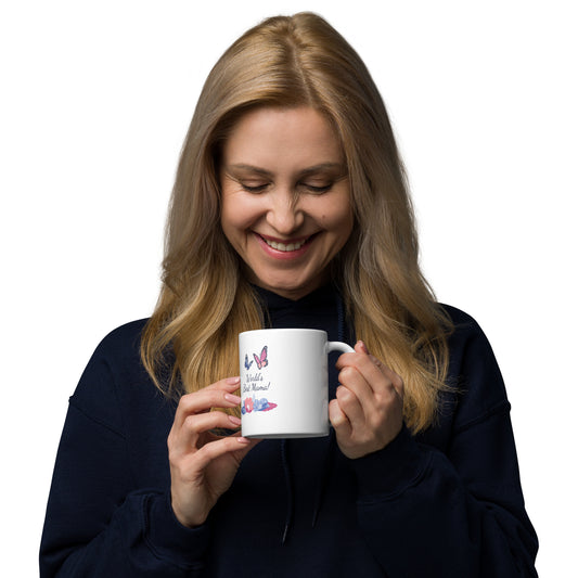 A smiling woman with long blonde hair in a dark hoodie holds a White glossy mug featuring butterflies and flowers, looking down at the dishwasher safe mug.